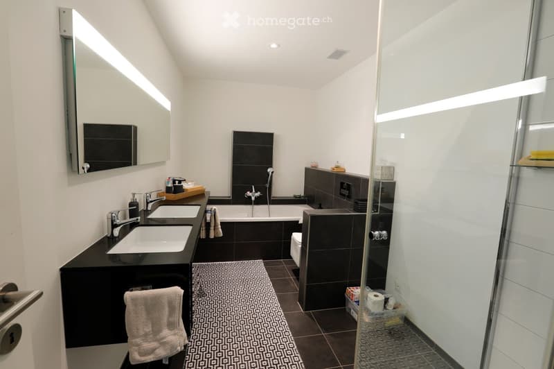 two sinks, large mirror, bathtub, toilet, walk-in shower, rug, towel on rack