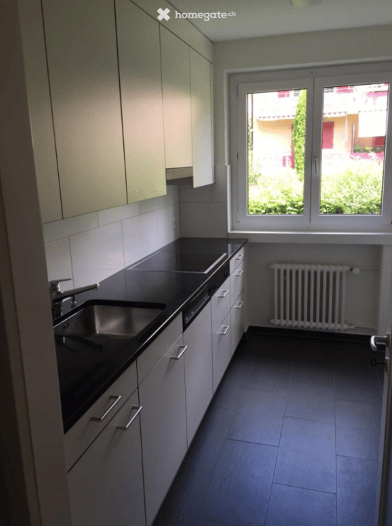 Modern kitchen with white cabinets, black countertops, stainless steel sink, and a window overlooking a green area.
