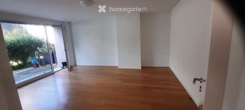 Empty room with wooden flooring, white walls, and large sliding glass door leading to outdoor area.