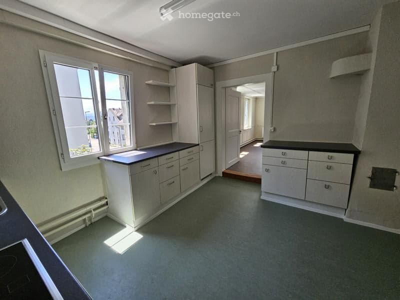 Empty kitchen with white cabinets, black countertops, and a window letting in natural light. No appliances or furniture are present.