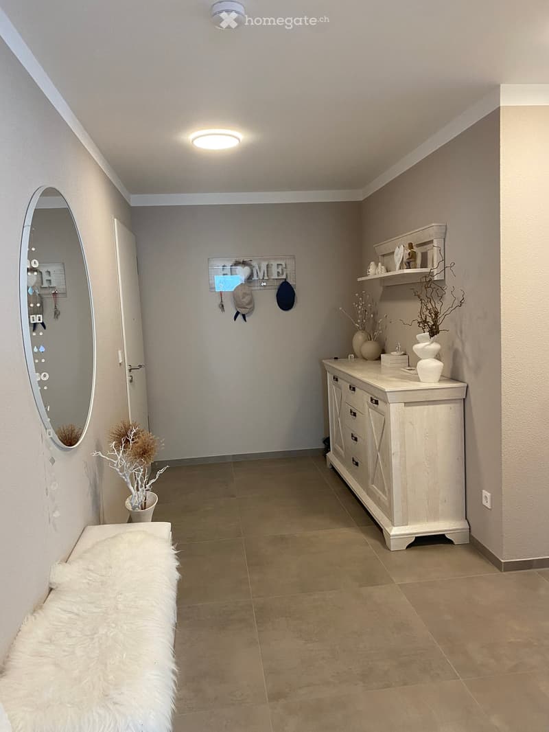 Modern hallway with tiled floor, white walls, built-in storage unit, decorative vases, and a fur throw on a bench.