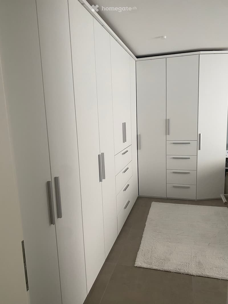 Empty room with white built-in wardrobes, grey handles, and a white shag rug on a tiled floor.