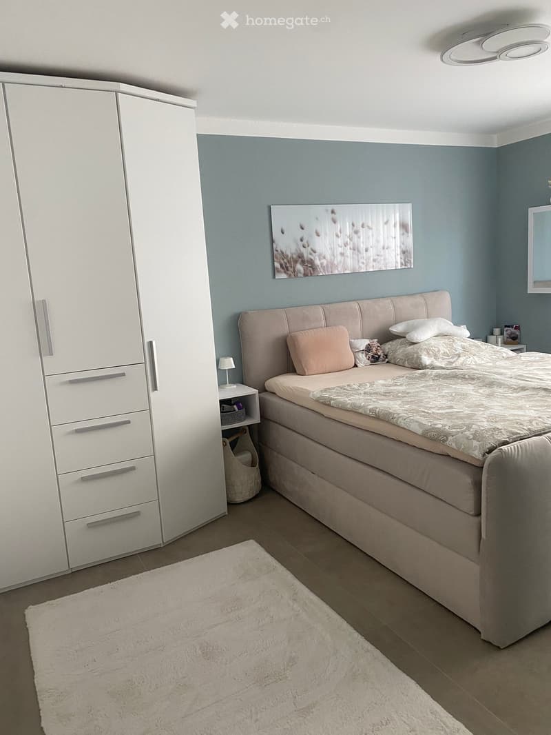 Modern bedroom with a large bed, white wardrobe, nightstand with lamp, and a decorative picture on the wall.