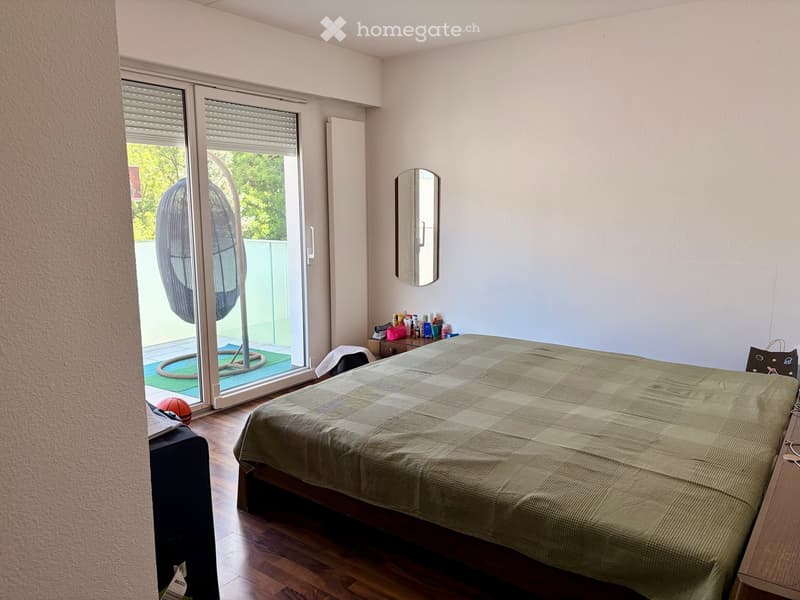 Bedroom with a large bed, a mirror on the wall, a nightstand, a ball near the sliding glass door, and a chair near the bed.
