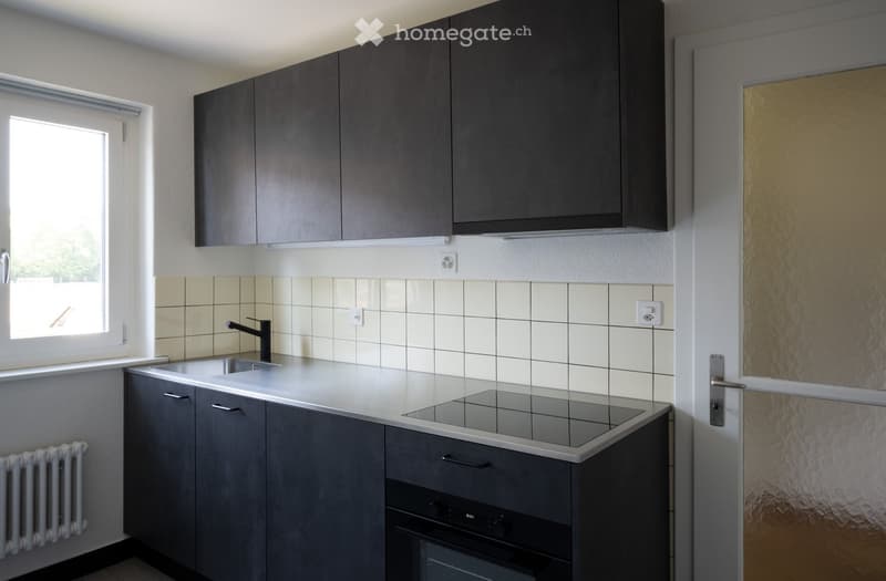 Modern kitchen with dark grey cabinets, white tiled backsplash, induction cooktop, sink, and oven.