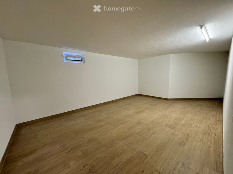 Empty room with wooden flooring and white walls, featuring a small window and a ceiling light fixture.