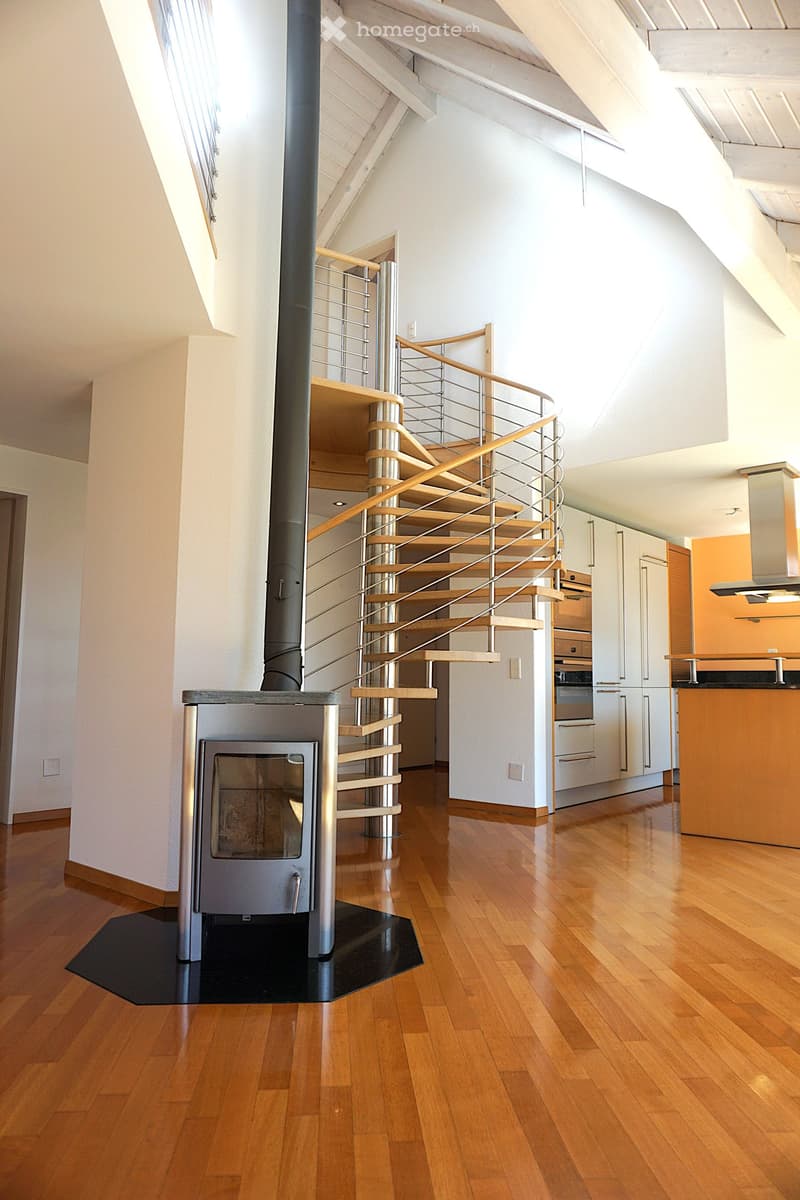 Modern interior with a wooden staircase, a central fireplace, and a kitchen area featuring cabinets and an island.