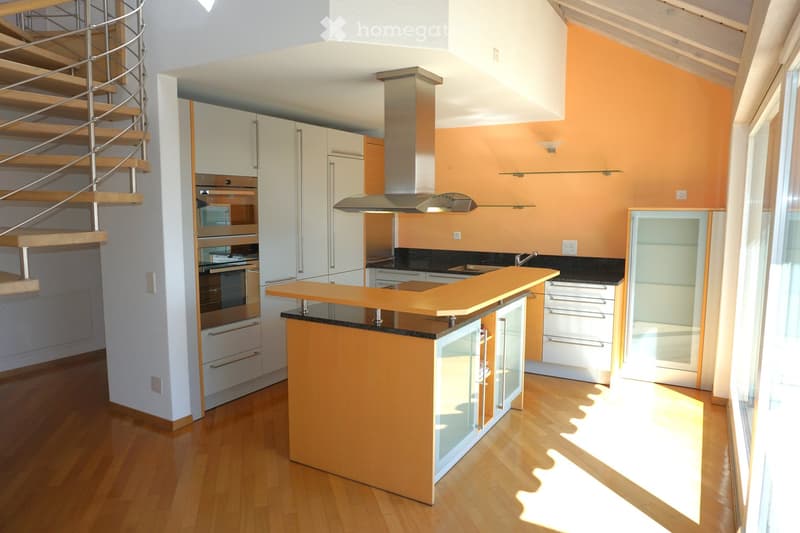 Modern kitchen with white cabinets, a central island, built-in appliances, and a spiral staircase leading to an upper level.