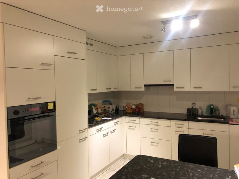 Modern kitchen with white cabinets, black granite countertop, built-in oven, and various appliances.