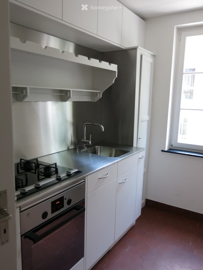 Modern kitchen with white cabinets, stainless steel appliances, gas stove, sink, and a window providing natural light.
