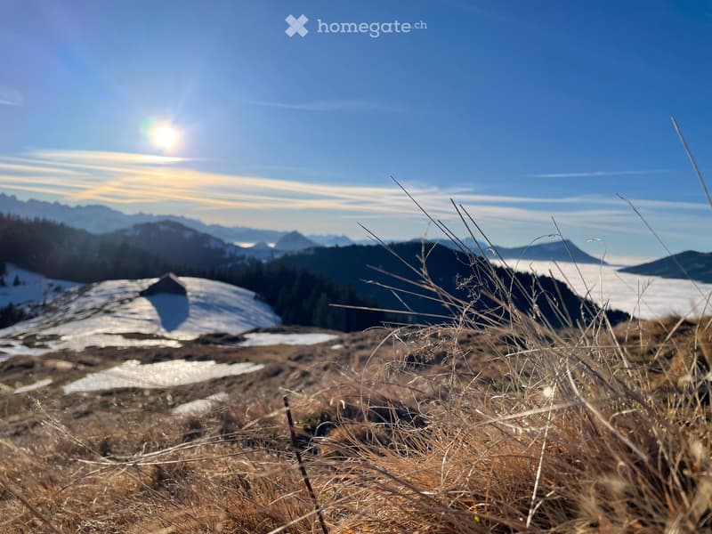 A serene mountain landscape with snow-covered peaks, a clear blue sky, and a small structure partially visible in the distance.
