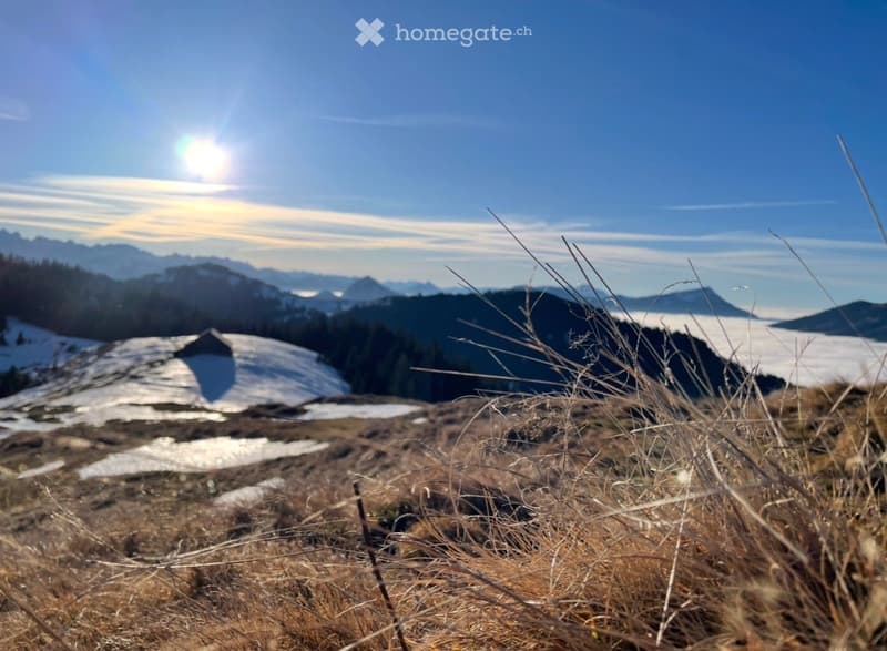 A serene mountain landscape with snow-covered peaks, a clear blue sky, and a small cabin nestled among trees.
