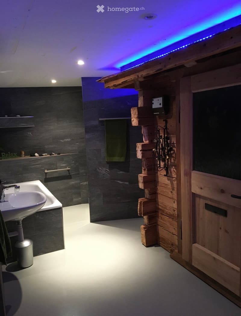 Modern bathroom with dark grey tiles, wooden accents, a sink with a chrome faucet, and a built-in shelf with decorative items.