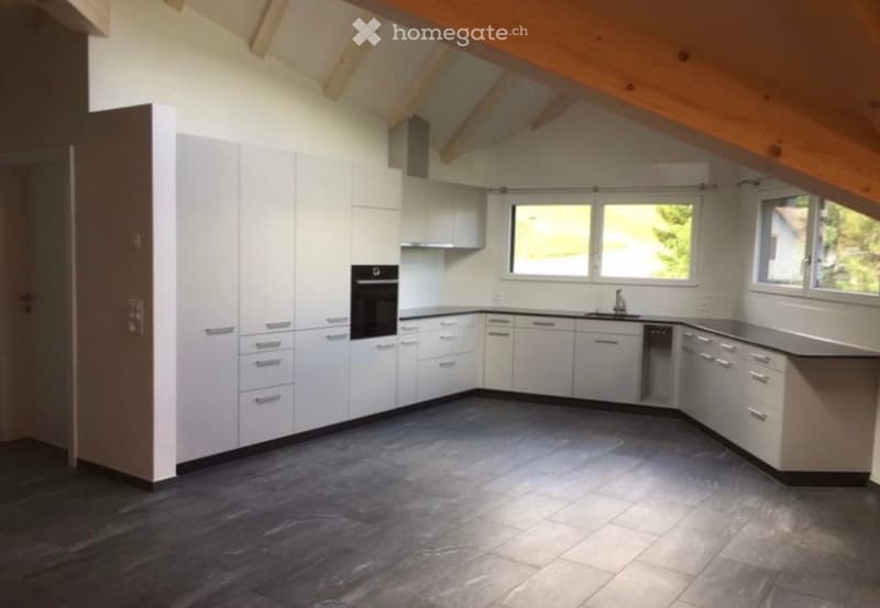 Modern kitchen with white cabinets, stainless steel appliances, dark tiled floor, and large windows allowing natural light.