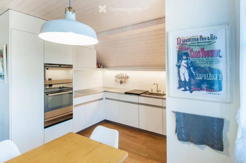Modern kitchen with white cabinets, stainless steel oven, wooden dining table, and a large pendant light.