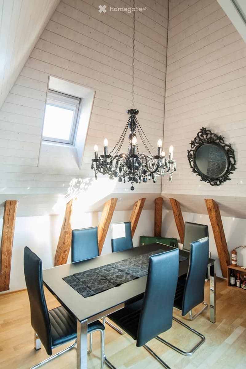 Dining room with a modern glass table, blue chairs, chandelier, and a decorative mirror on the wall.