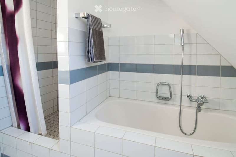 Modern bathroom with white tiles, a bathtub, a towel rack with a towel, and a showerhead.