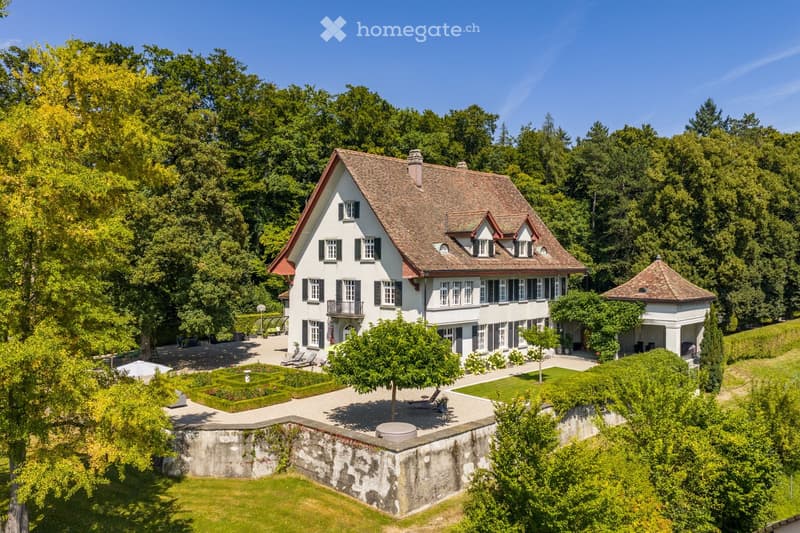 A two-story white house with a red-tiled roof, surrounded by a well-maintained garden and lush greenery.