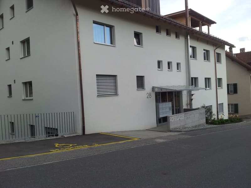 A multi-story residential building with white walls, multiple windows, and a small entrance area marked "Rufgasse".