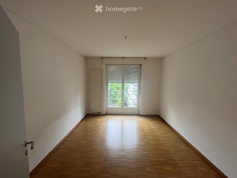 Empty hallway with wooden flooring, white walls, and a glass door leading to a balcony area.