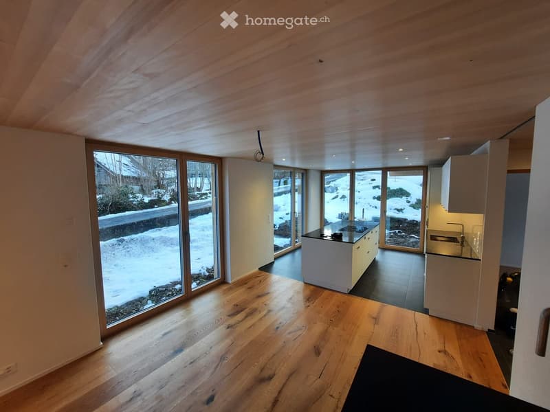 Modern kitchen with light wood flooring, white cabinets, and large windows overlooking a snowy outdoor area.