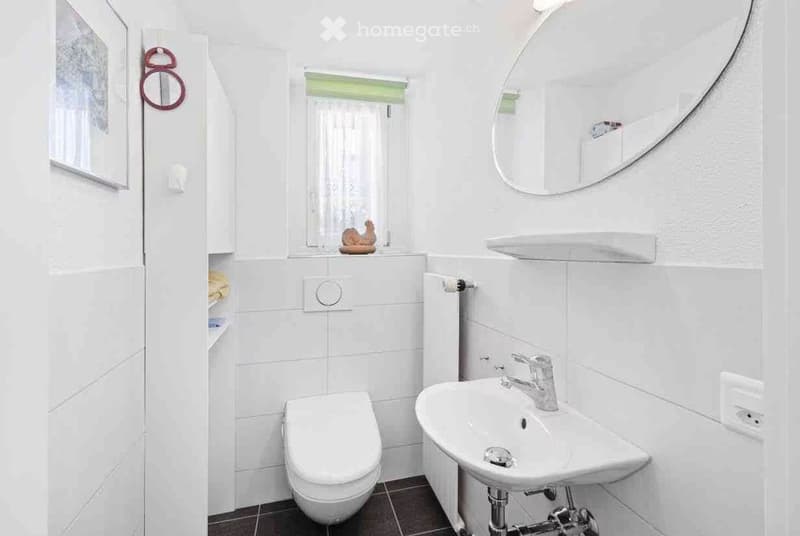 Modern white bathroom with a toilet, sink, mirror, and cabinet. The sink has a modern chrome faucet, and the walls are tiled in white.