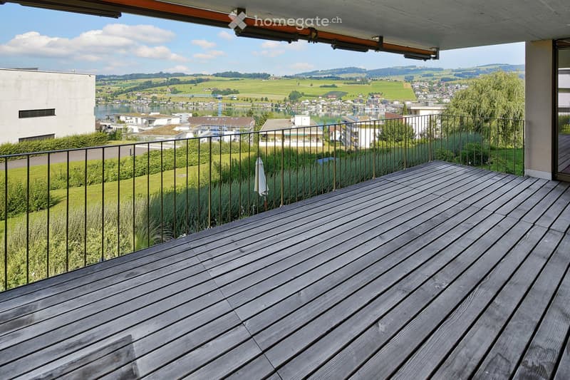 Wooden deck with metal railing, overlooking a scenic landscape with fields, water, and distant hills.