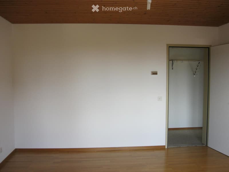 Empty room with wooden flooring, white walls, and a closet with a rod for hanging clothes.