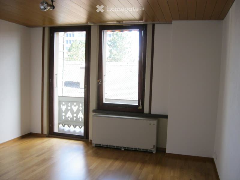 Empty room with wooden flooring, white walls, large window, and a door leading to a balcony.