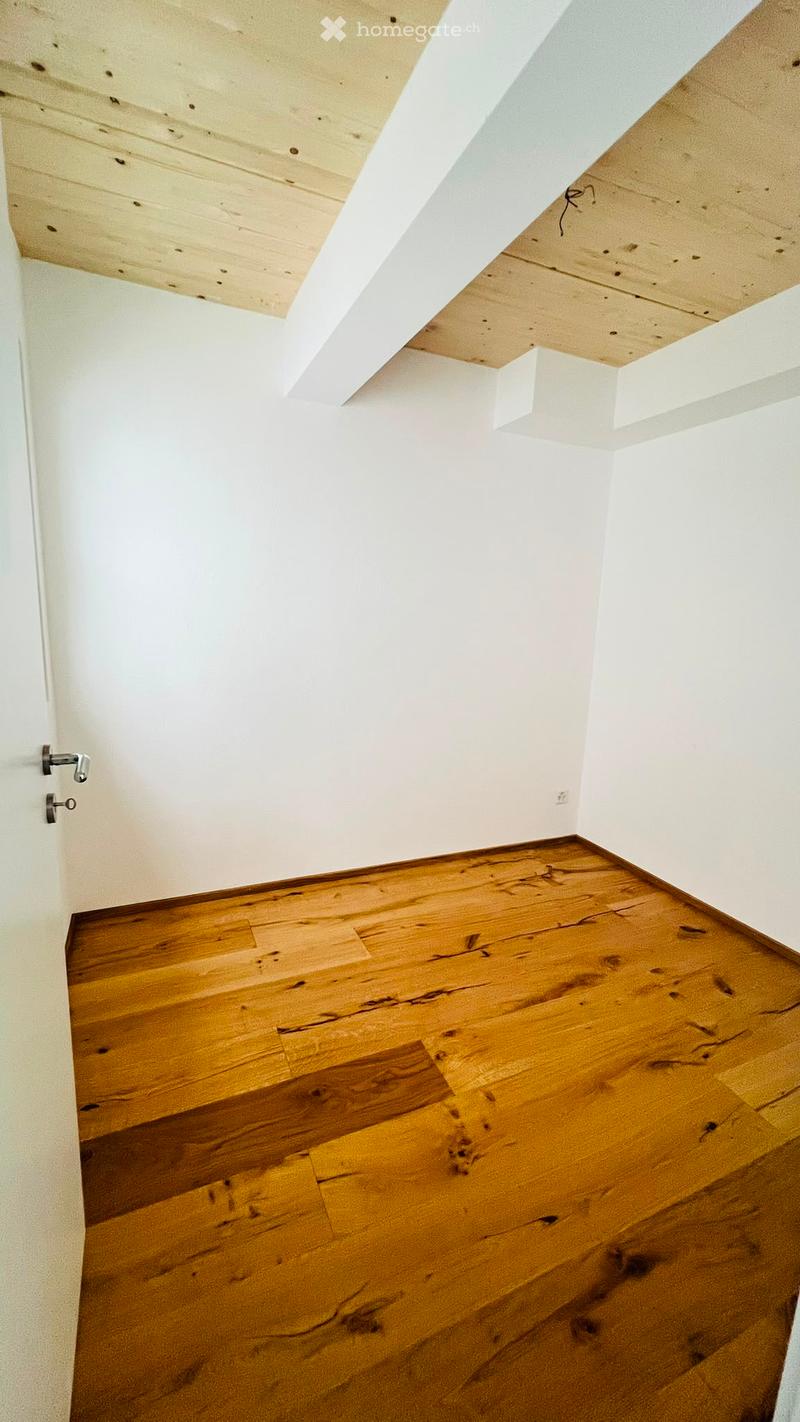 Empty room with wooden flooring and white walls, featuring a visible door frame and ceiling beams.