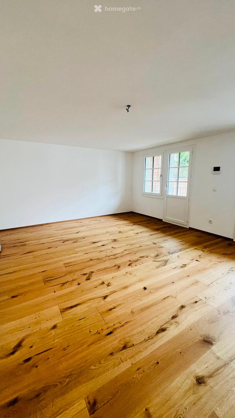 Empty room with light wooden flooring and white walls, featuring a white door with glass panels and a small window.