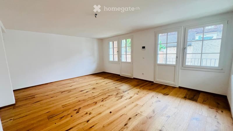 Empty room with wooden flooring, white walls, and multiple windows, including a door leading outside.