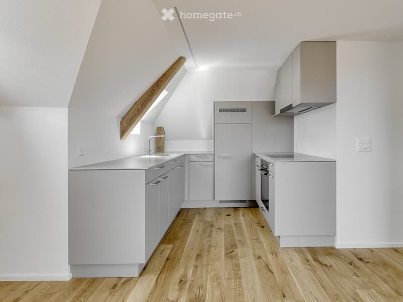 Modern kitchen with light grey cabinets, white countertops, wooden flooring, and built-in appliances including a sink, oven, and range hood.