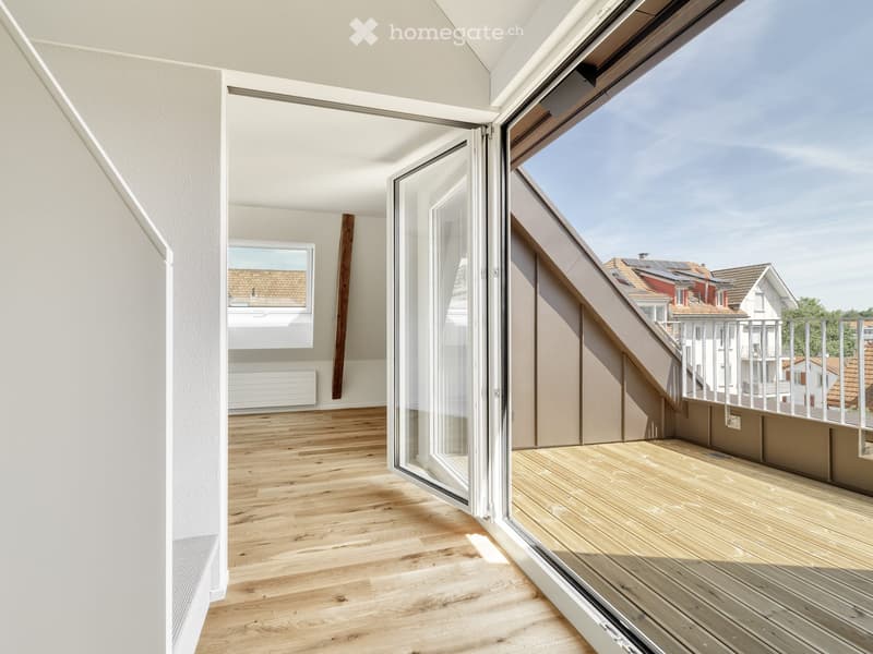 Modern balcony with wooden decking, glass sliding doors, and a view of neighboring buildings.