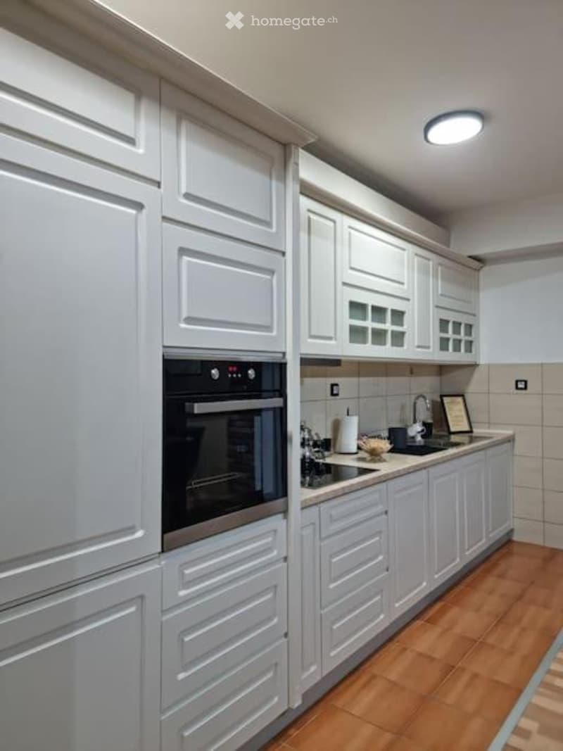 Modern kitchen with white cabinets, wooden flooring, built-in oven, and a sink with a faucet.