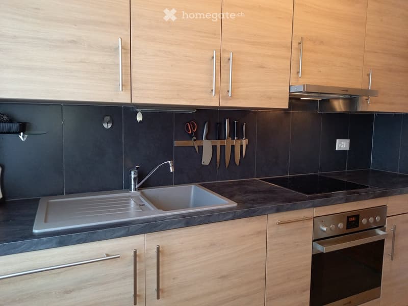 Modern kitchen with light wooden cabinets, stainless steel sink, oven, and knives hanging on the wall.