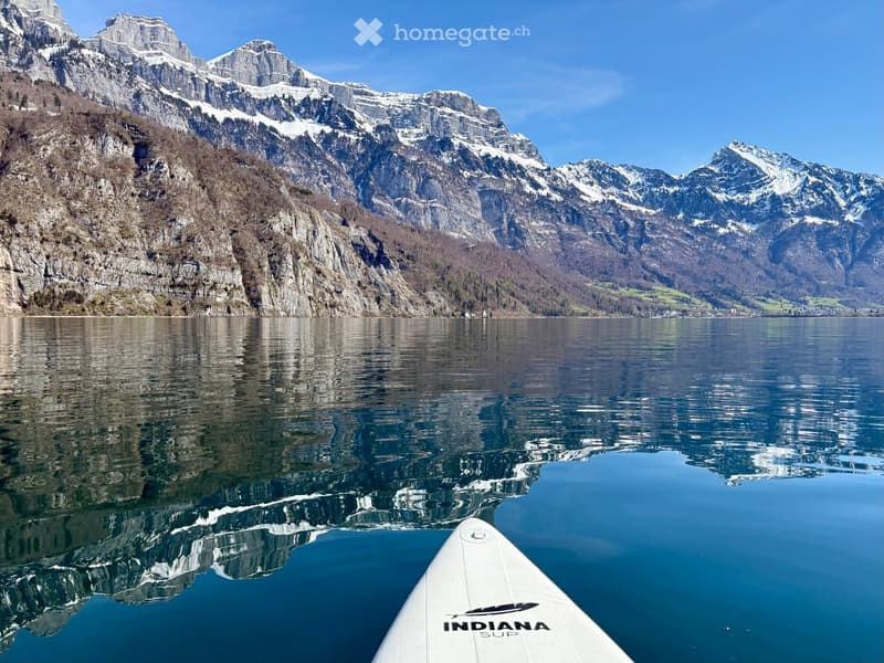 A serene lake surrounded by snow-capped mountains, with a paddleboard in the foreground reflecting the landscape.