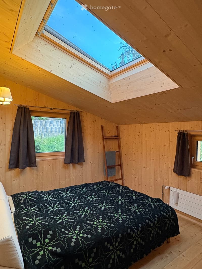 Cozy attic bedroom with wooden walls, skylight, bed with patterned quilt, radiator, ladder, and curtains.