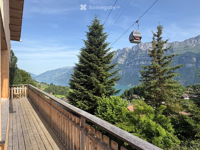 Wooden balcony with railing, overlooking a scenic mountain lake and cable car.