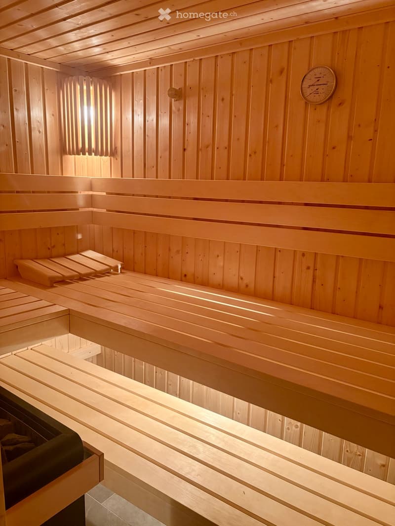 Wooden sauna with multiple benches and a thermometer on the wall.