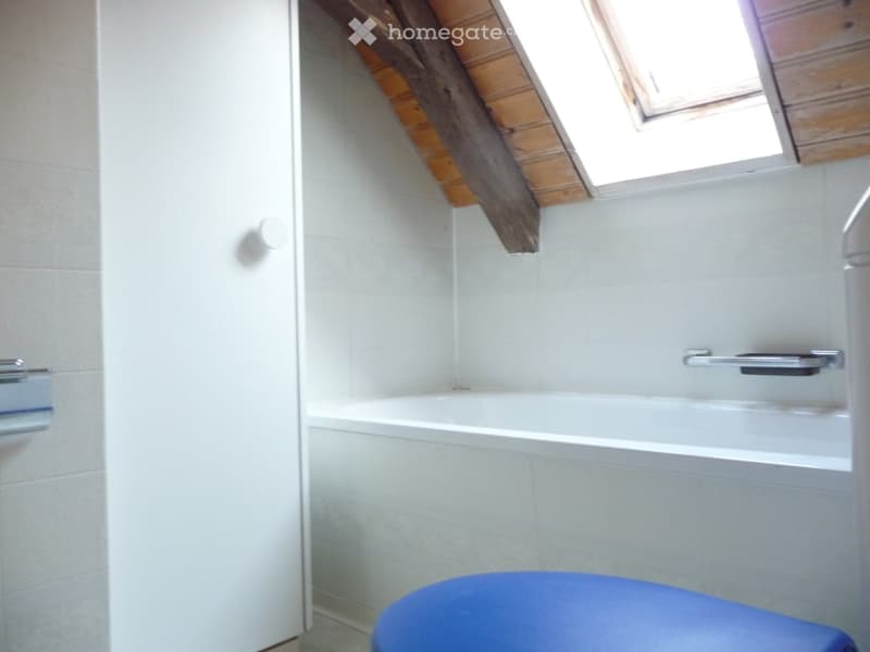 A small bathroom with a white tiled wall, a bathtub, a toilet, and a skylight window above the bathtub.