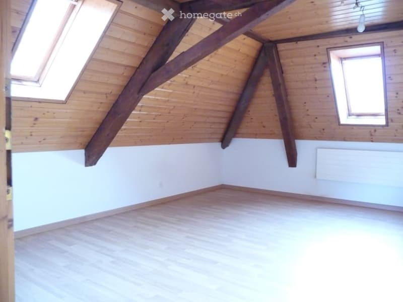 Empty attic room with wooden beams, wooden floor, and skylights. No furniture or equipment present.