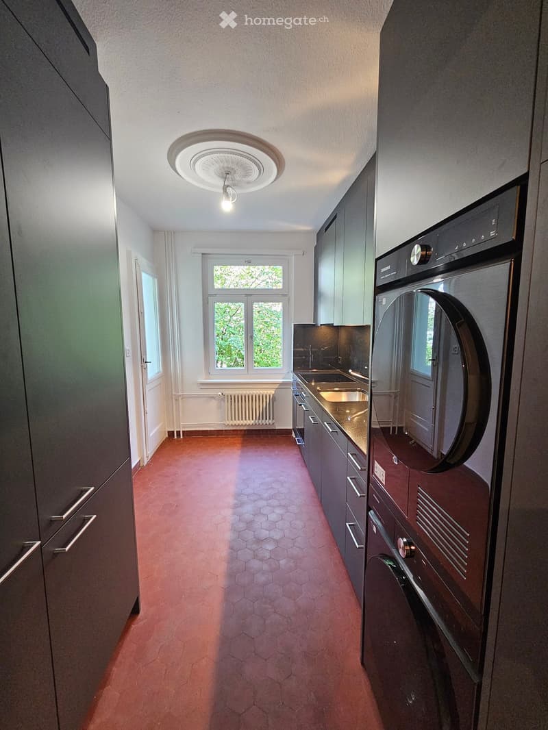 Modern kitchen with dark grey cabinets, stainless steel sink, and a red hexagonal tile floor.