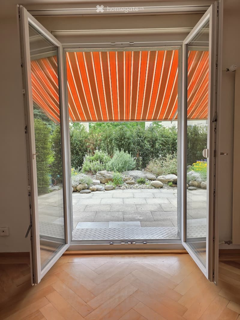 Open sliding glass doors lead to a landscaped garden with rocks, plants, and a paved patio.