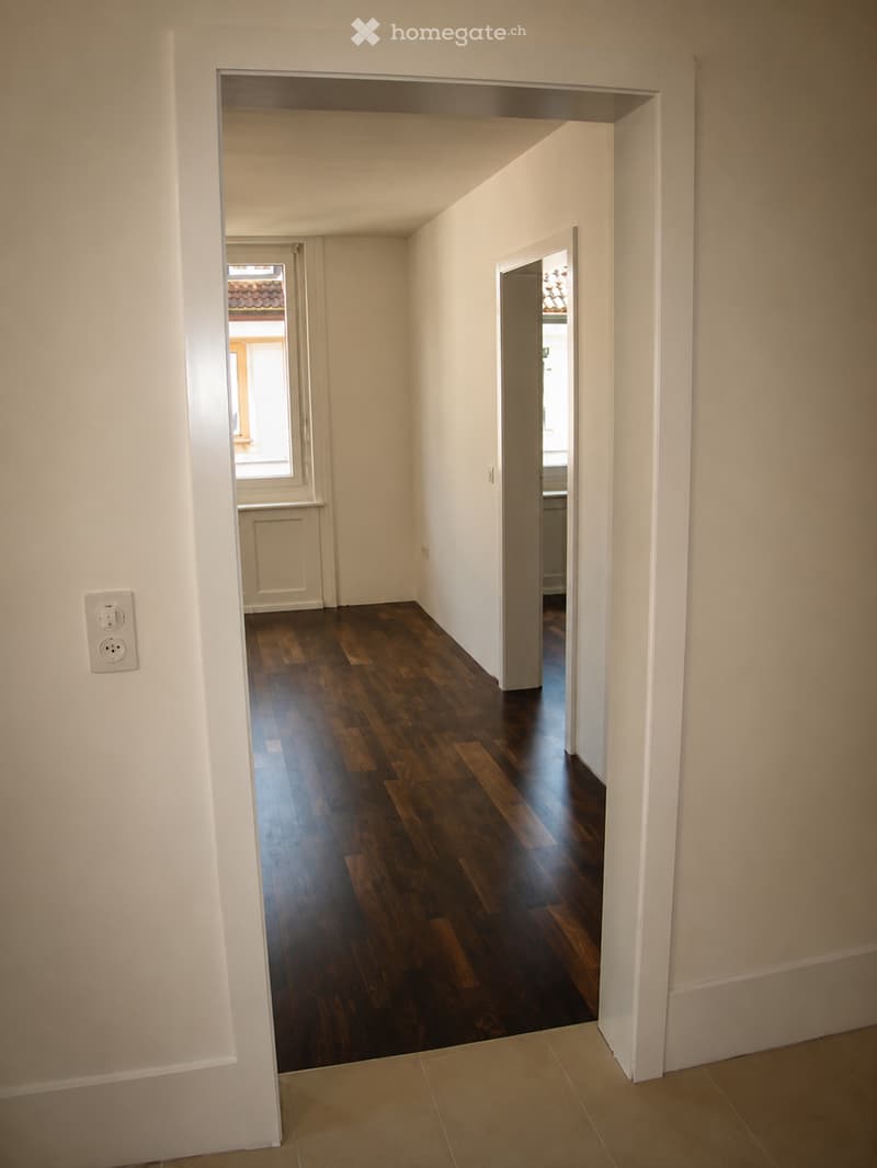 Empty hallway with wooden flooring, white walls, and multiple doorways leading to other rooms.