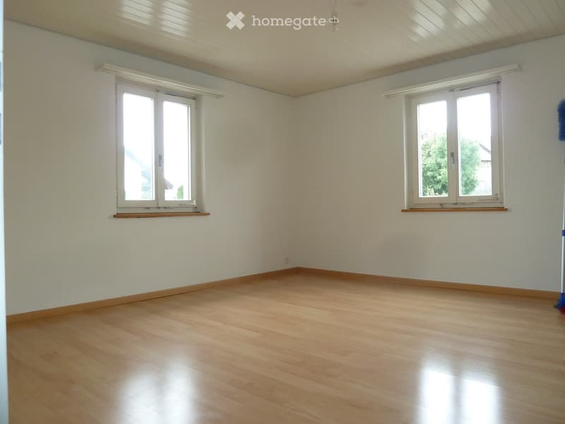 Empty room with light wooden flooring, white walls, and two windows with white frames and wooden sills.
