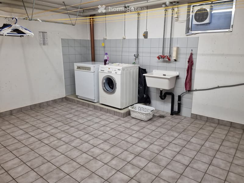 Laundry room with tiled floor, white washing machine, dishwasher, sink, and laundry basket.