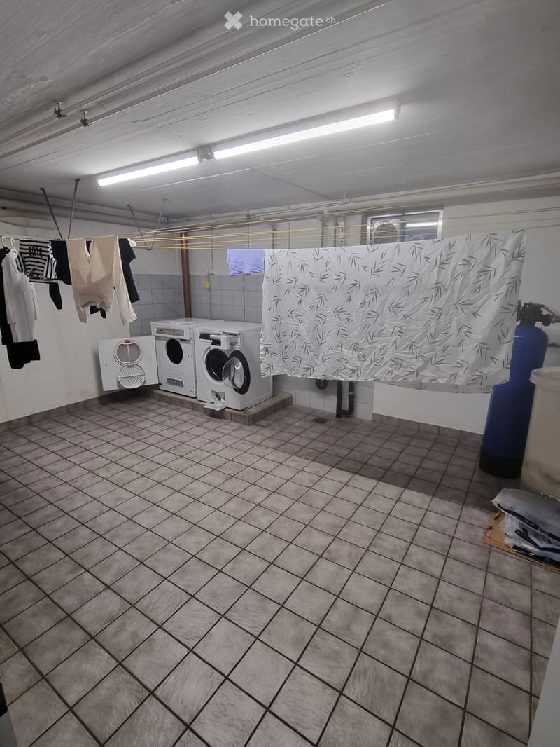 Laundry room with tiled floor, white washing machine, dryer, and clothes hanging on a rack.