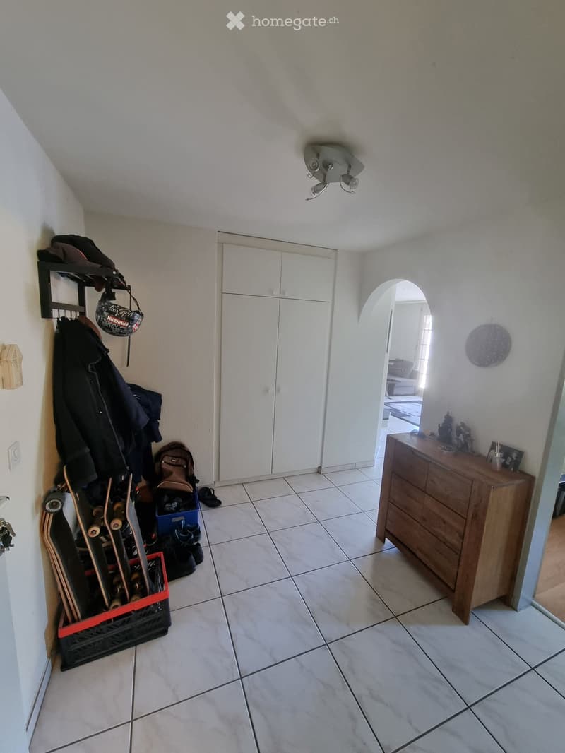 Hallway with tiled floor, white walls, coat rack with jackets, storage cabinet, and a wooden dresser with decorative items on top.