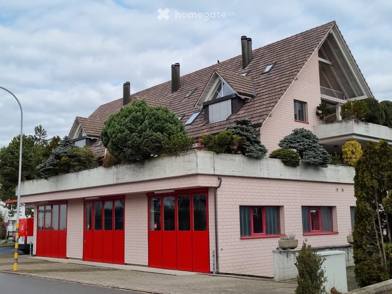 Two-story house with pink brick facade, red garage doors, multiple windows, and a balcony on the upper level.